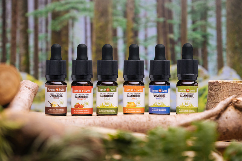 Kuus Formula Swissi täisspektriga CBD-õli eri kandeõlide ja maitsetega metsa taustal